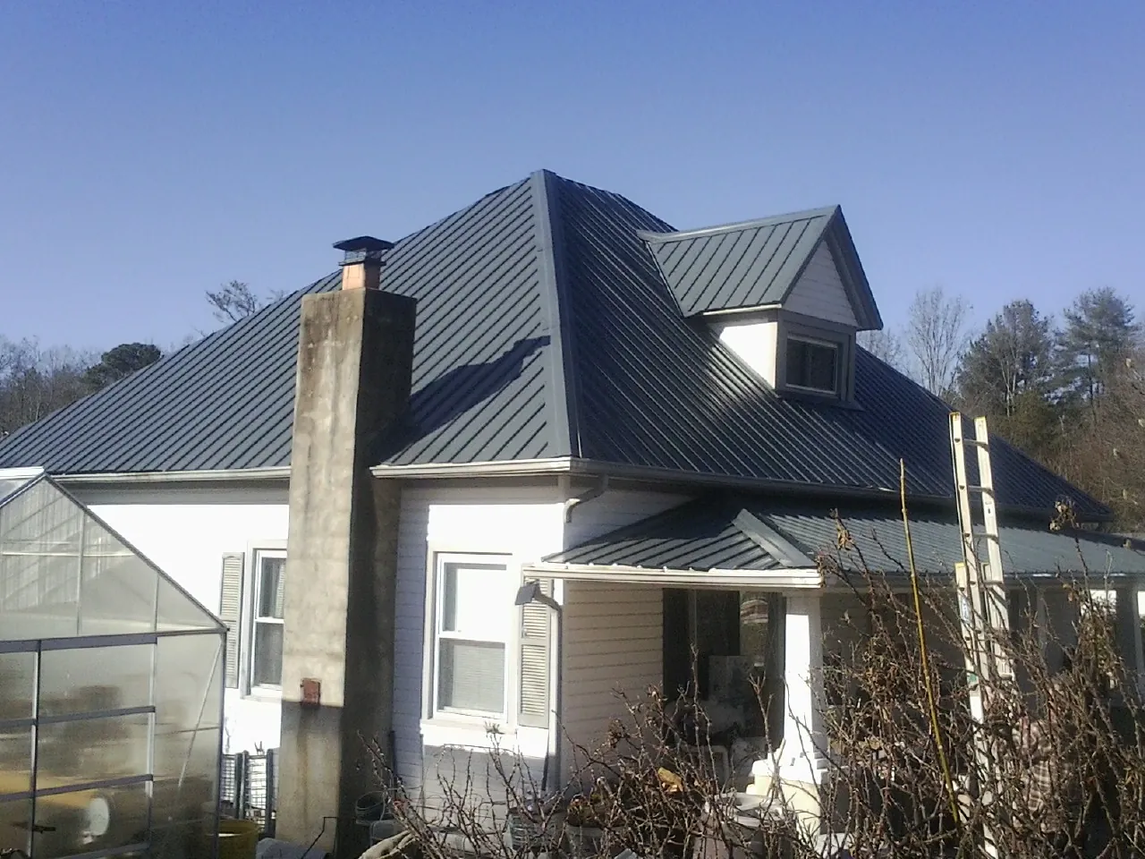 Dark blue standing seam metal roof on a white farmhouse with dormer — Slate & Tile Roof Repair by Roofing Brothers in Crescent