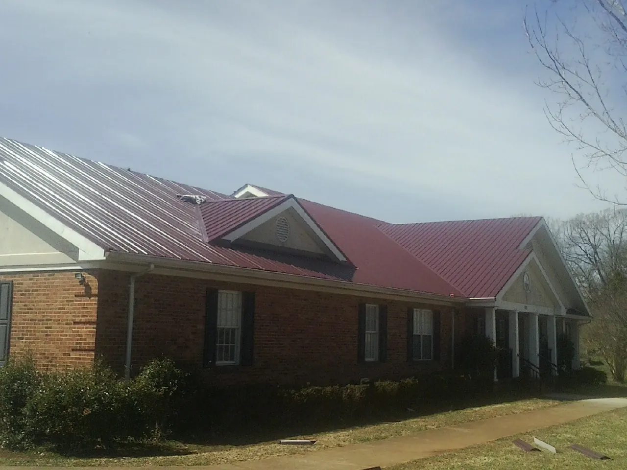 Red metal roof with gabled entries on a long brick building, from a Hail Damage Roof Repair job in Crescent