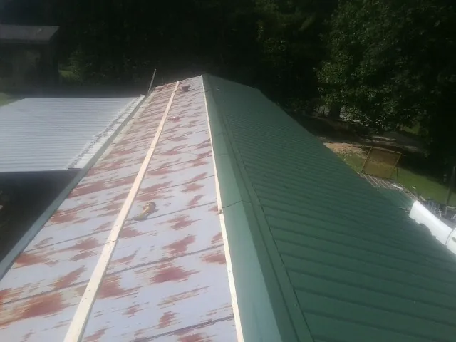 Old rusted panels beside newly installed green metal roofing — Wind Damage Roof Repair by Roofing Brothers in Crescent