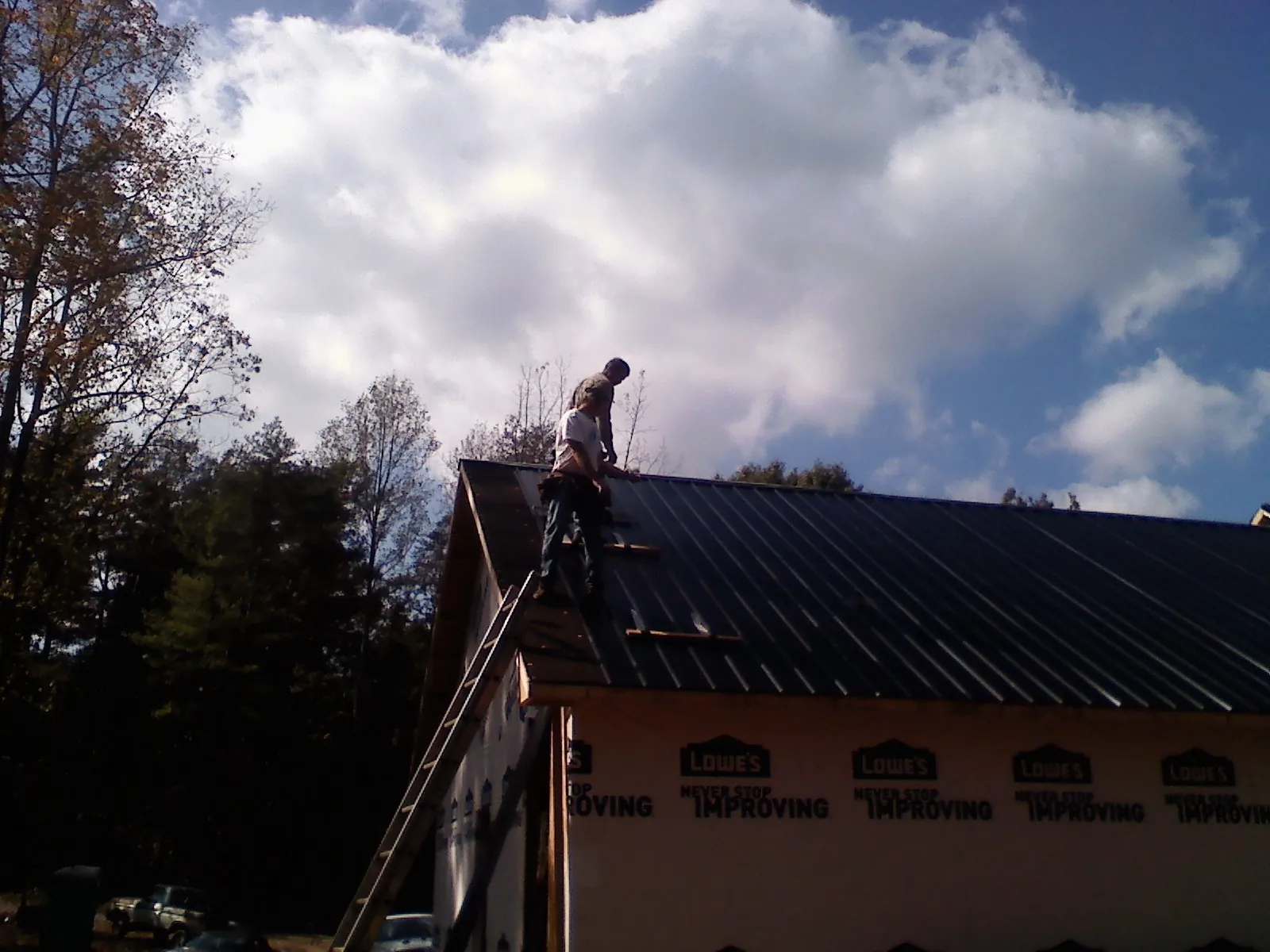 Roofer fastening dark metal panels high against a cloudy sky, from a Roof Inspection job in Crescent