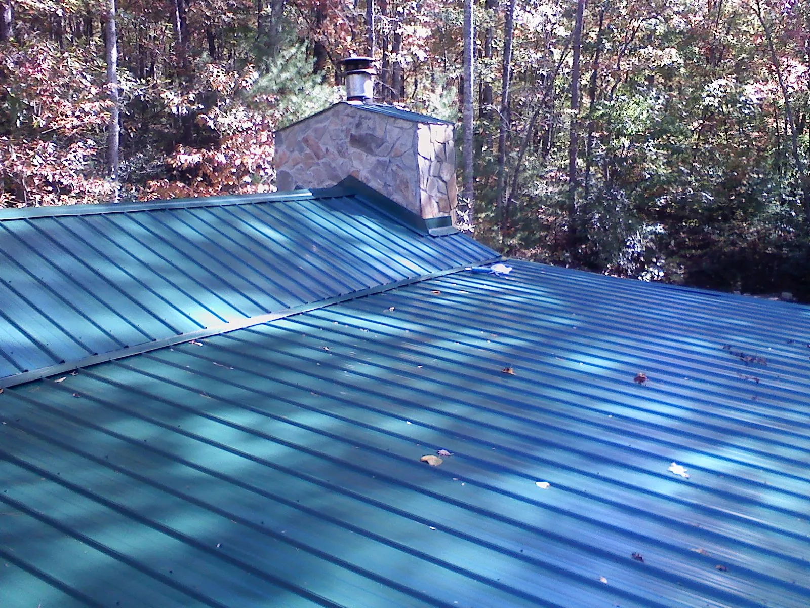 New green metal roof and stone chimney surrounded by autumn woods in Crescent
