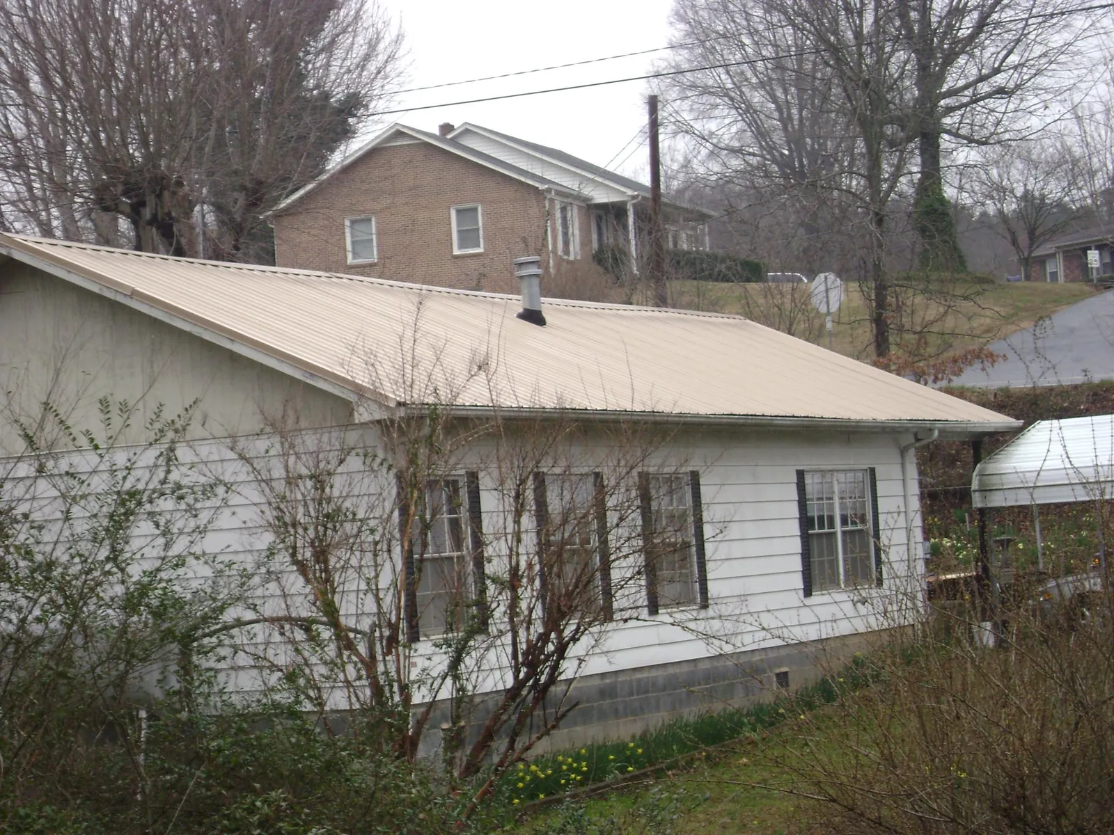 Tan metal roof on a white sided house set into a hillside — Commercial Roofing by Roofing Brothers in Crescent